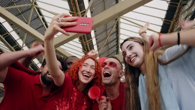 Group of fans taking a selfie while cheering for their sports team from a stadium. Cheerful male and female fans recording a video with their phone while watching the game at the stadium.