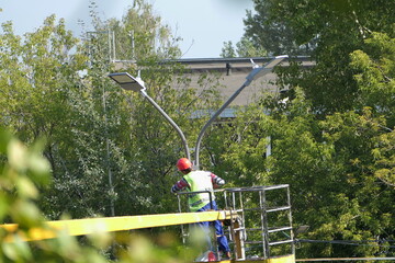 Street lamps on poles. A man in special clothes and a helmet on his head repairs a street lamp on a pole.