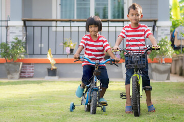 Little cute asian boy and girl on bikes, looking at camera, sister and brother on playground at home