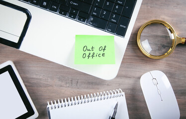 Out of office message on sticky note with computer.