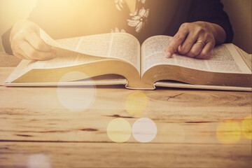 Close up of a woman hand hold and pointing on an open bible, blurred page on wooden table with window light and Bokeh, Christian devotional, spiritual or bible study concept background with copy space