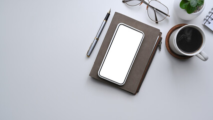 Mock up smart phone with blank screen, notebook and coffee cup on white desk.