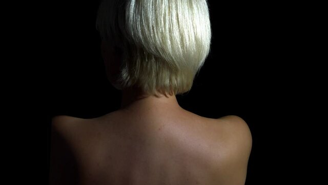 A beautiful woman standing naked and turn around looking at camera. An elegant female with a short hairstyle posing for a moment with a happy expression. A relaxed naked lady turn around her head.