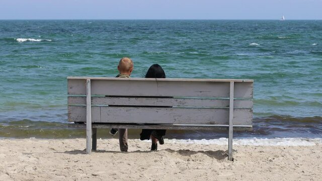 Happy couple are sitting on a wooden bench andand relaxing view of the sea on a sunny day. Back view
