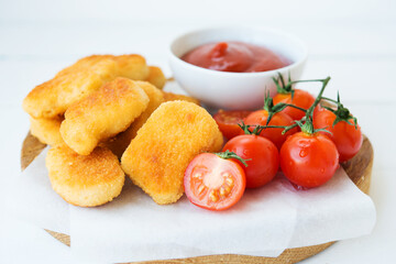Homemade chicken nuggets with sauce and tomatoes on a wooden board