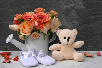 Teddybär mit Babyschuhen und Blumenstrauß.
