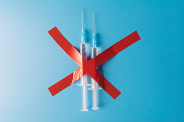Two syringes crossed with red tapes over blue background. Vaccine refusal concept