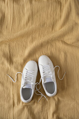 White female sneakers on yellow crumpled muslin cloth background. Flat lay, top view. Merchandise, marketing, sale, shopping concept