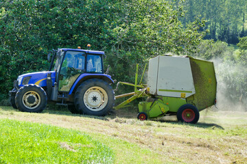 Tractor pulling a baler over lines of dry cut hay to make hay bales for animal fodder
