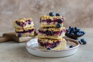 Crumble cheesecake bars with blueberry filling and fresh blueberries, concrete background. Bar slices with cheesecake, blueberry and streusel.