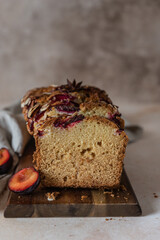Homemade spicy plum cake decorated with almond on a wooden serving board, concrete background. Loaf cake with plum, spices and almond.