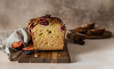 Homemade spicy plum cake decorated with almond on a wooden serving board, concrete background. Loaf cake with plum, spices and almond.
