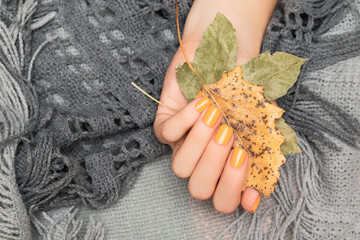 Female hand with glitter orange autumn nail design. Female hand hold autumn leaves. Woman hand on...