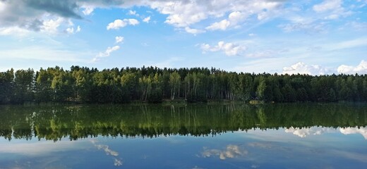 Flat lake, against the background of a forest and a clear, blue sky