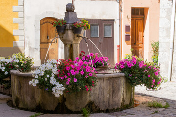 Old stone fountain decorated with flowers with pink, white and yellow petunias in Colmars-les-Alpes...
