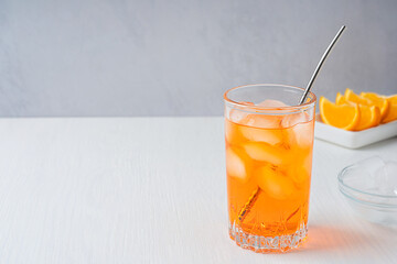 Glass of cold refreshing orange carbonated drink served with metal straw, ice cubes and citrus...