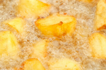 Potato is frying in cauldron in oil on nature on fire, closeup view. Large pieces of potatoes are deep-fried in a black kazan. Cooking using wood-burning stove.