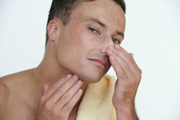 Naklejka premium Handsome attractive young man touching his face looking for imperfections, wrinkles and pimples