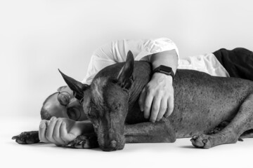 Black and white pic of young stylish male in formal shirt lying down on the floor, hugs dogs...