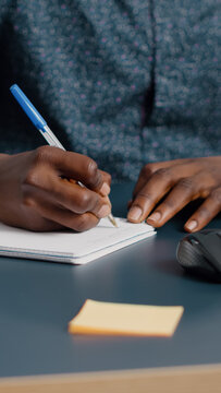 Closeup African American Black Man Hands Taking Notes On Notepad Using A Pen. Male Adult Hands Of Remote Worker Writing Text On White Paper. Business Student In Home Office Handwriting Documents