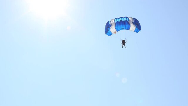 Parachute on the blue sky. Parachutist is flying slowly down with an open parachute. Skydiving, gliding, parachute jump