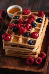 Fresh homemade Belgian waffles on an old wooden table with raspberries, blueberries and honey.