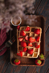 Fresh homemade Belgian waffles on an old wooden table with strawberries and honey.