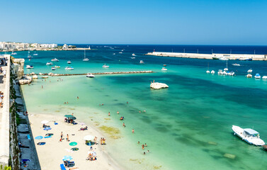 Panoramic view of the seaside and the beach of Otranto seen from the bastion of the castle, with moored boats, bathers and parasols, in Otranto, Salento area, province of Lecce, Puglia, Italy
 - obrazy, fototapety, plakaty