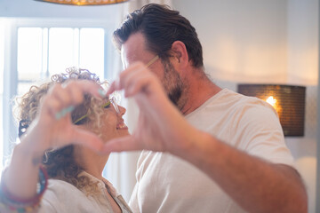 Happy adult couple in love do heart sign with hands - relationship people enjoy home together -...