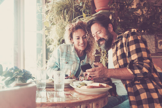 Happy adult couple enjoy bar restaurant break leisure indoor together using modern cell phone to video call friends or looking for on the web - online modern people wireless connection