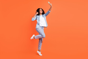 Fototapeta na wymiar Full size photo of funky young brunette lady do selfie thumb up wear jeans shirt shoes isolated on orange background
