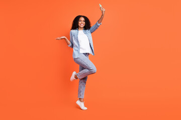Fototapeta na wymiar Full size photo of cool young brunette lady do selfie wear jeans shirt shoes isolated on orange color background