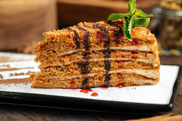 Slice of sweet honey cake with cacao powder on wooden background