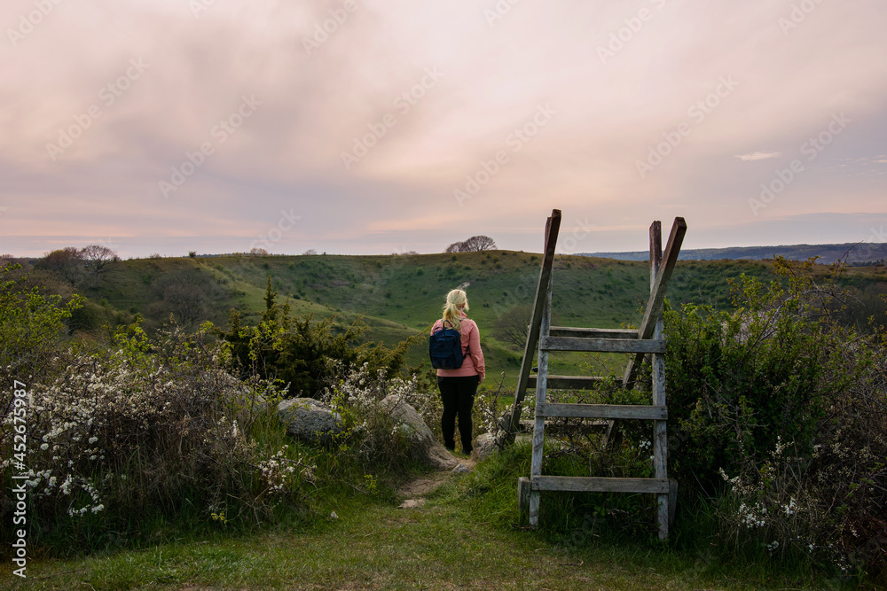 Wall mural woman hiking during sunset in the countryside landscape in skåne, sweden. woman wearing outdoor clot