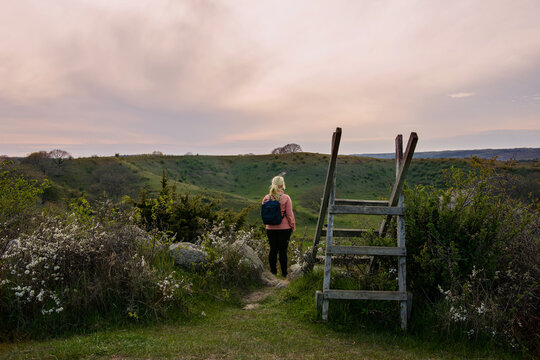 Woman hiking during sunset in the countryside landscape in Skåne, Sweden. Woman wearing outdoor clothing with a pink wind jacket and a backpack. Photo taken at Brösarps Backar, Österlen
