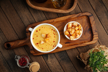 Yellow chicken cream soup with croutons in a white bowl on rustic background