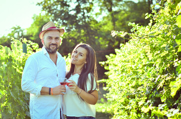 Fototapeta premium Portrait of a smiling happy couple kissing in a Vineyard toasting wine. Beautiful brunette woman and bearded muscular man spending time together