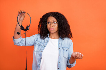 Photo of sad millennial brunette lady hold headphones wear jeans shirt eyewear isolated on orange...