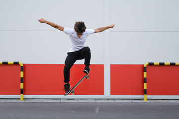 young skater does tricks outdoor. background is white and red wall