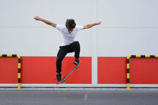 young skater does tricks outdoor. background is white and red wall