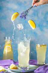 Glasses of lavender lemonade with splash and fly cube ice and lavender flowers in woman hand on the...