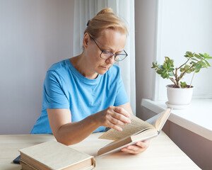 A mature woman reads with glasses a book leafs through the pages, pensioner studies, gains new knowledge