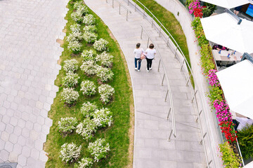 Two girls are walking in the park. People walk along the path in the city modern park. A place to relax with a summer cafe and entertainment