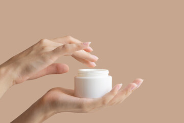 Woman's hand dips her finger into mock-up of white package with cream. Concept of body care, beauty industry.