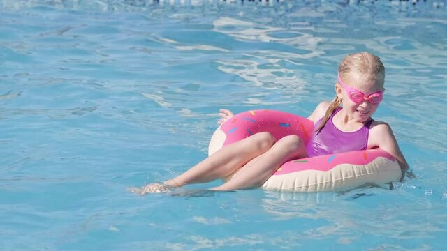 Portrait smiling girl in swimming pool, child in swimming glasses sitting on pink donut swimming ring. Summer travel family hotel vacation tourists