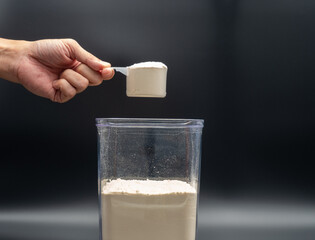 Whey protein powder in  scoop hold by hand. Supplements for bodybuilders, sportmans and healthy eating.