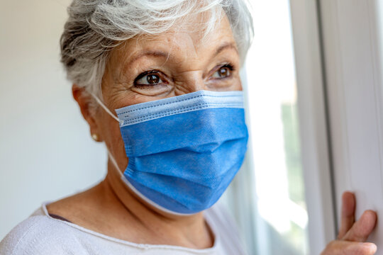 Side view of a caucasian senior woman is wearing a protective face mask in front of a window. Shot of a senior woman wearing a face mask in a hospital. New normal life. Healthcare and medicine concept