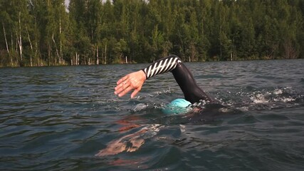 Triathlon swimmer preparing for the race. Athletic Young man swimming in wetsuit.  professional triathlete swim practicing at the lake