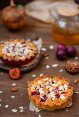 Plum pies on a shortbread basis with frangipan and almond petals on a wooden background with plum decor top view.