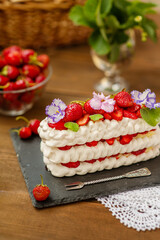 Pavlova dessert with strawberries and violet flowers as a decor on a wooden background